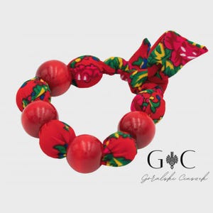 Pode incluir: Uma pulseira de contas vermelhas com detalhes em tecido. A pulseira apresenta grandes contas vermelhas brilhantes e contas cobertas de tecido. O tecido tem um fundo vermelho com um padrão floral em verde, amarelo e rosa. Um laço de tecido é amarrado no topo.