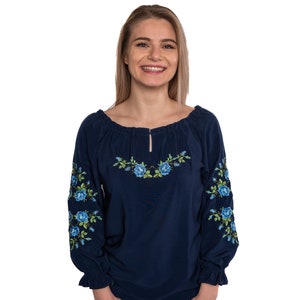 May include: A navy blue embroidered blouse with a floral design. The embroidery features blue and green flowers. The blouse has a round neckline and long sleeves.