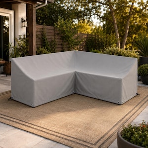 May include: A light gray L-shaped outdoor furniture cover designed to fit a sectional sofa. The cover features a smooth, solid-colored fabric surface with visible metal grommets along the bottom edge for securing the protective material.