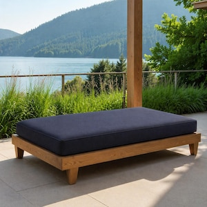 May include: A rectangular outdoor daybed with a navy blue cushion and a light brown wooden frame. The daybed is on a patio with a scenic view of a lake and mountains in the background.