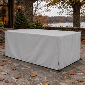 May include: A rectangular, light gray outdoor furniture cover made of a smooth, solid-colored fabric. The cover features clean, straight seams along the edges and a small, dark rectangular brand tag attached to the lower side panel.
