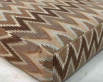 Puede incluir: Un cojín rectangular con un patrón de chevrón repetitivo en tonos marrón, beige, crema y azul claro. La tela tiene una apariencia suave y texturizada con un diseño de zigzag consistente que cubre las superficies superior y lateral del objeto.
