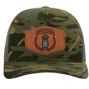 May include: A camouflage baseball cap with a brown leather patch. The patch features the text "FIRELINE EXPLOSIVES" above a bomb graphic, surrounded by a laurel wreath. The cap has a mesh back and a curved brim.
