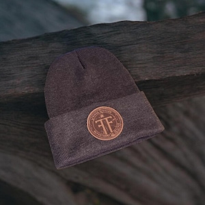 May include: A dark gray beanie with a brown leather patch featuring the text "Fire Division Department of Engine 1" and a stylized "FF" logo.