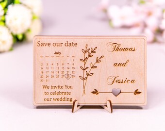 Puede incluir: Una tarjeta de madera para guardar la fecha con un calendario que muestra el 28 de julio marcado. La tarjeta está grabada con el texto "Save our date", "Thomas y Jessica", y "We invite you to celebrate our wedding".