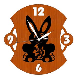 Op de afbeelding: Een houten wandklok met een zwart konijnen silhouet dat een paasei vasthoudt. De wijzerplaat van de klok heeft witte cijfers en wijzers. De klok is bruin met een houtnerfstructuur.