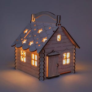 May include: A wooden house shaped nightlight with a handle on top. The house has a roof with cut-out stars and windows with warm yellow lights. The house is made of wood and has a rustic look.