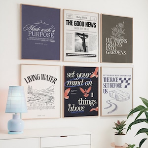 May include: A collection of framed art prints with inspirational quotes and religious themes. The prints feature various designs, including text, illustrations, and a newspaper-style layout. The color palette includes navy, white, and black, with a light blue lamp in the foreground.