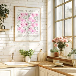 May include: A framed print with a floral pattern of pink roses and green foliage. The print displays the text "PHILIPPIANS 4:13" and "I CAN DO ALL THINGS THROUGH CHRIST WHO STRENGTHENS ME". It is mounted on a white brick wall.