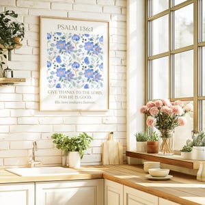 Op de afbeelding: Een ingelijste print met de tekst "PSALM 136:1" en een bloemmotief van blauwe bloemen en groene bladeren. De tekst "GIVE THANKS TO THE LORD, FOR HE IS GOOD, His love endures forever" staat eronder. De print bevindt zich in een keuken.