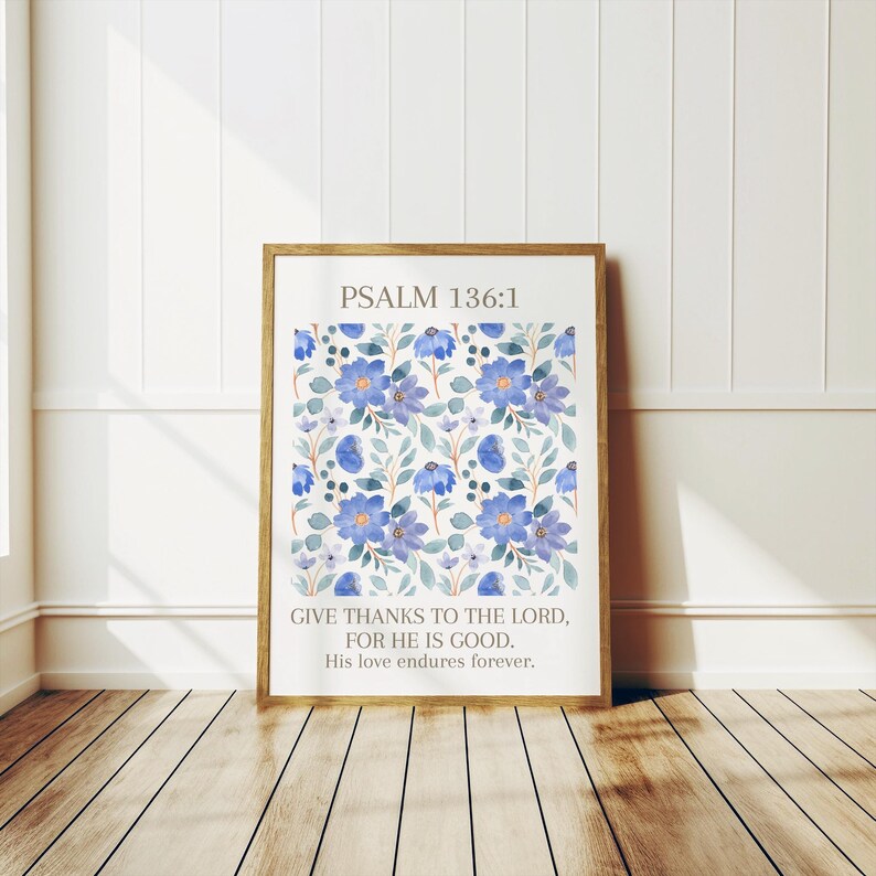 Op de afbeelding: Een ingelijste print met een aquarel bloemenpatroon in blauwe en groene tinten. De print bevat de tekst "PSALM 136:1" en een bijbelvers. De lijst is lichtbruin en de print wordt gepresenteerd op een houten vloer.