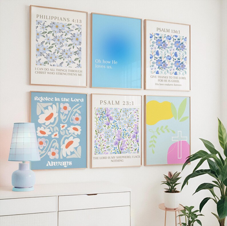 Op de afbeelding: Een verzameling ingelijste kunstprints met bloemen en abstracte ontwerpen in pastelkleuren. De prints bevatten tekst, waaronder bijbelverzen. Een blauwe lamp en potplanten staan op de voorgrond.