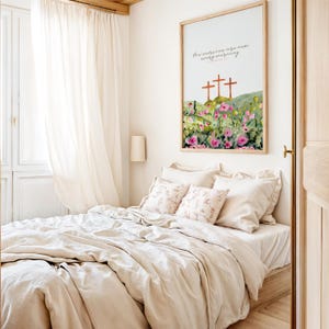 Pu&ograve; includere: Una camera da letto con un letto con lenzuola beige e cuscini decorativi. Un'opera d'arte incorniciata con croci e fiori &egrave; appesa sopra il letto. Tende trasparenti e una porta in legno completano la scena.