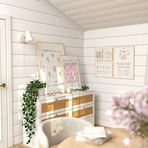 May include: A light and airy room featuring framed floral art prints with botanical illustrations and inspirational quotes. A white dresser with a woven front holds candles and greenery. A light fixture and a door are visible.