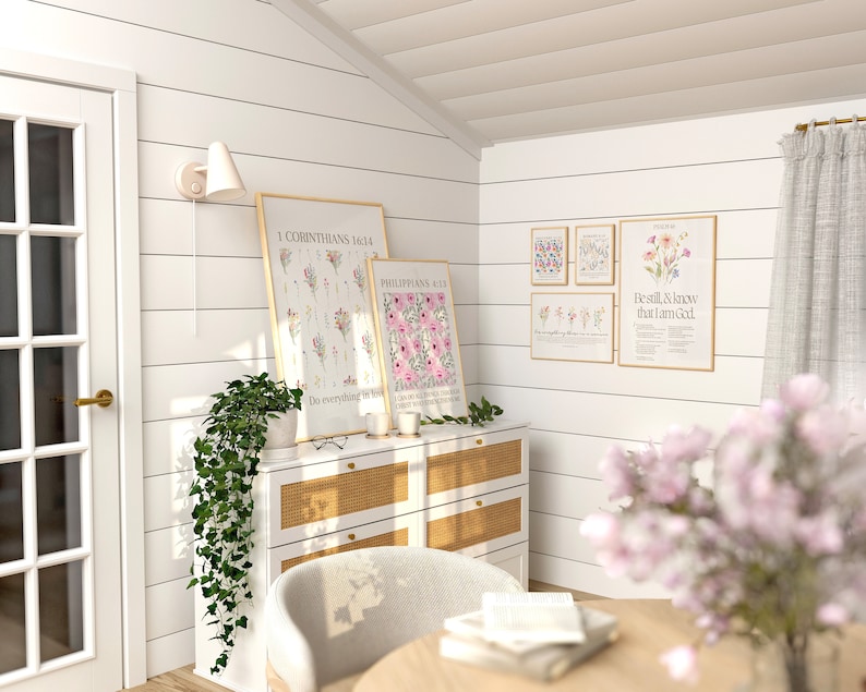 May include: A light and airy room featuring framed floral art prints with botanical illustrations and inspirational quotes. A white dresser with a woven front holds candles and greenery. A light fixture and a door are visible.
