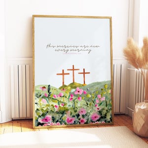 Pu&ograve; includere: Una stampa ad acquerello incorniciata con tre croci su una collina verde, circondate da fiori rosa e vegetazione. Il testo "His mercies are new every morning" &egrave; scritto in corsivo. La cornice &egrave; in legno chiaro.