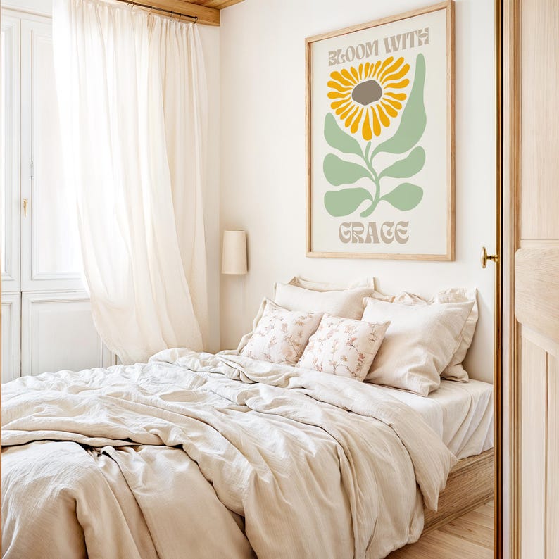 May include: A bedroom scene featuring a bed with beige bedding and floral pillows. A framed poster on the wall displays a sunflower illustration with the text "BLOOM WITH GRACE". The room has a light and airy feel with sheer curtains.