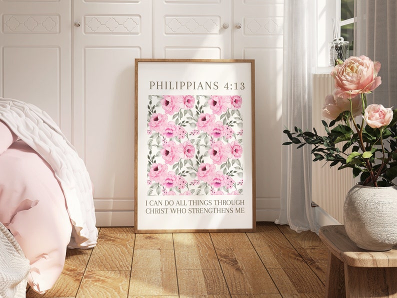 May include: A framed print with a floral design of pink roses and green leaves on a white backdrop. The text reads "PHILIPPIANS 4:13" at the top, with "I CAN DO ALL THINGS THROUGH CHRIST WHO STRENGTHENS ME" underneath. The frame is light brown.