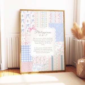 May include: Framed artwork featuring a patchwork design in pastel pinks, blues, and white. The artwork includes the text "Philippians 4:6-7" and a related Bible verse. The frame is a light brown color.
