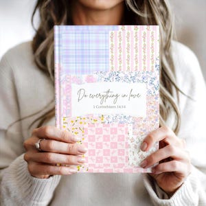 May include: A hardcover journal with a patchwork design in pastel colors. The cover features various floral and plaid patterns in pink, blue, and yellow. The text "Do everything in love" and "1 Corinthians 16:14" are displayed on a white banner.