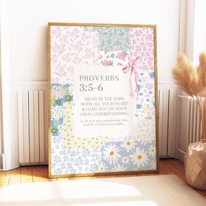 Op de afbeelding: Een ingelijste print met een patchwork-ontwerp van bloempatronen in roze, blauw en wit. De tekst "SPREUKEN 3:5-6" wordt weergegeven, samen met een citaat over vertrouwen in de Heer. Een roze lint voegt een decoratief tintje toe.