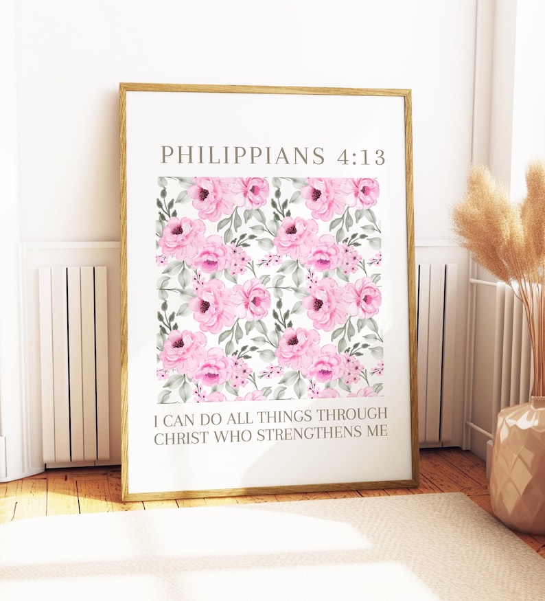 May include: A framed print with a floral design of pink watercolour roses and green leaves on a white backdrop. The text "PHILIPPIANS 4:13" is at the top, with "I CAN DO ALL THINGS THROUGH CHRIST WHO STRENGTHENS ME" below the floral design. The frame is gold.