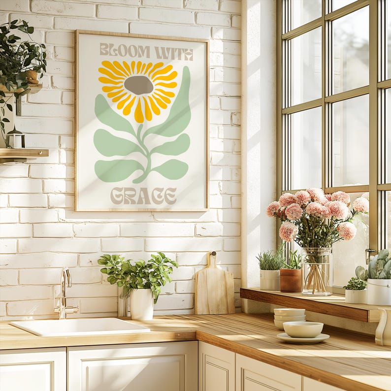 May include: A framed art print with a sunflower design and the words "BLOOM WITH GRACE" in a kitchen setting. The sunflower has yellow petals and a brown center, with green leaves and a light background.