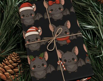 Op de afbeelding: Zwart cadeaupapier met een herhaald patroon van cartoonvleermuizen met feestelijke accessoires zoals kerstmutsen, strikken en sjaals. Het cadeau is vastgebonden met touw en geplaatst tegen een achtergrond van dennennaalden en dennenappels.