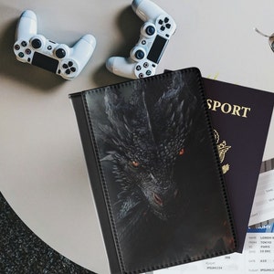 Peut inclure: Porte-passeport noir avec un motif de dragon. Le dragon a des yeux rouges et est sur un fond sombre. Le porte-passeport a une bordure cousue.