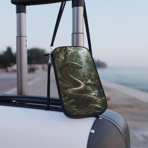 May include: A rectangular crossbody bag featuring a detailed graphic print of a large snake coiled in a lush, green jungle environment. The bag has a black border, a thin black adjustable strap, and silver-toned metal hardware clips.