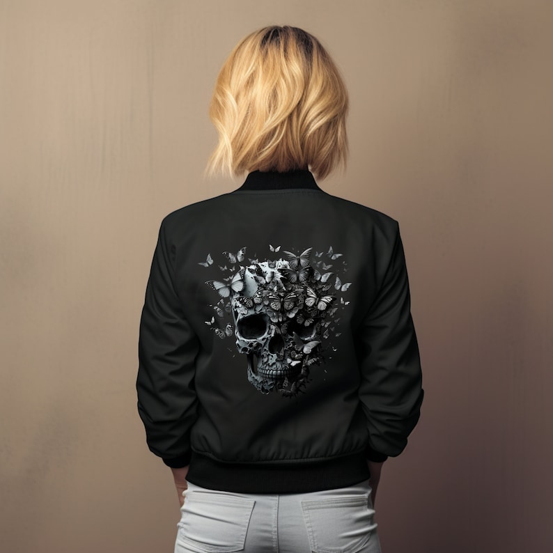 May include: Black bomber jacket featuring a detailed skull design composed of butterflies. The jacket has a classic bomber silhouette with a ribbed collar, cuffs, and hem. The skull and butterfly graphic is in shades of gray and white.