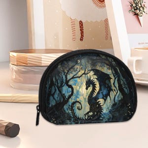 May include: A black, half-moon shaped coin purse featuring a fantasy dragon design. The dragon is black with blue accents, set against a backdrop of a moonlit forest. The purse has a black zipper.