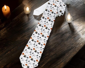 May include: White Halloween necktie with a repeating pattern of black cats, orange pumpkins, bats, and stars. The tie is displayed on a dark wooden surface with lit candles in the background.