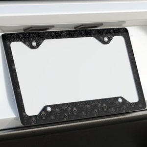 May include: Black license plate frame with a skull pattern. The frame is made of durable plastic and has a sleek, modern design.