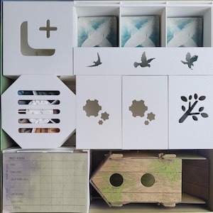 May include: A white game board with a wooden birdhouse, a score sheet, and various compartments with cutouts of birds, flowers, and a tree branch. The board is labeled "MULTI-PLAYER".