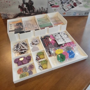 以下が含まれることがあります： ゲームの駒を収納するための白いプラスチック製のオーガナイザー。オーガナイザーには、カード、トークン、小さな部品用のコンパートメントがあります。オーガナイザーには、カード、トークン、小さな部品など、さまざまなゲームの駒が収納されています。