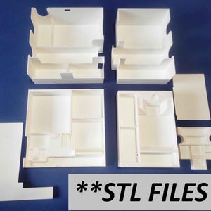 Puede incluir: Un conjunto de seis cajas de almacenamiento de plástico blanco con varios compartimentos. Las cajas están diseñadas para guardar objetos pequeños, como piezas de juego o cartas. **STL FILES** está impreso en la parte inferior de la imagen.
