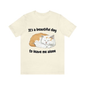 Könnte beinhalten: Ein beiges T-Shirt mit einer schlafenden weißen und orangefarbenen Katze. Der Text auf dem Shirt lautet "It's a beautiful day to leave me alone."