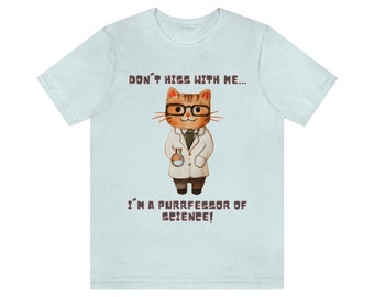 Op de afbeelding: Lichtblauw T-shirt met een cartoonkat die een bril en een labjas draagt. De tekst op het shirt luidt "Don't hiss with me... I'm a purrfessor of science!"
