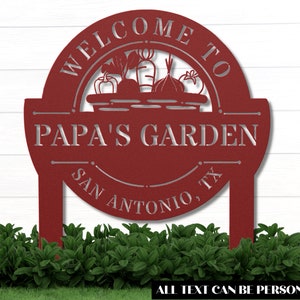 K&ouml;nnte beinhalten: Rotes Metall-Gartenschild mit dem Text "Willkommen im Garten von Papa San Antonio, TX". Das Schild zeigt eine Silhouette eines Gem&uuml;sekorbs.