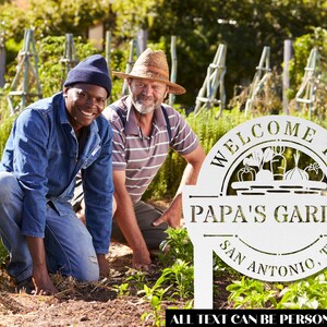 K&ouml;nnte beinhalten: Ein wei&szlig;es Garten Schild aus Metall mit dem Text "Willkommen im Garten von Papa San Antonio, TX". Das Schild zeigt einen Korb mit Gem&uuml;se und den Text "Alle Texte k&ouml;nnen personalisiert werden". Zwei Personen sind im Hintergrund, eine tr&auml;gt ein blaues Hemd und die andere einen Strohhut.