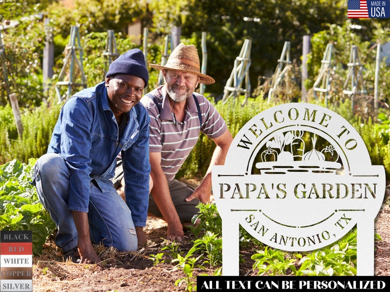 K&ouml;nnte beinhalten: Ein wei&szlig;es Garten Schild aus Metall mit dem Text "Willkommen im Garten von Papa San Antonio, TX". Das Schild zeigt einen Korb mit Gem&uuml;se und den Text "Alle Texte k&ouml;nnen personalisiert werden". Zwei Personen sind im Hintergrund, eine tr&auml;gt ein blaues Hemd und die andere einen Strohhut.