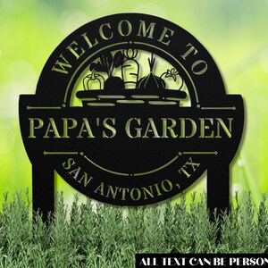 K&ouml;nnte beinhalten: Schwarzes Garten Schild aus Metall mit einem Willkommen im Garten von Papa Design. Das Schild zeigt einen Korb mit Gem&uuml;se und den Text San Antonio, TX. Der gesamte Text kann personalisiert werden.