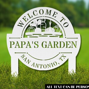 K&ouml;nnte beinhalten: Wei&szlig;es Garten Schild aus Metall mit einem Korb voller Gem&uuml;se und dem Text "Willkommen im Garten von Papa San Antonio, TX". Der Text kann personalisiert werden.