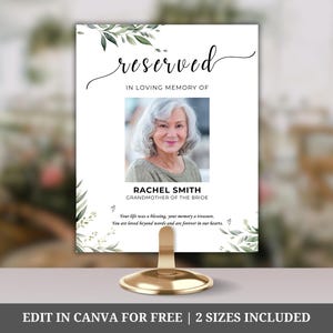 May include: A white table card with green foliage border, the text "reserved" in cursive, and the words "In loving memory of" above a photo of a woman. The text below the photo reads "Rachel Smith, Grandmother of the Bride". The text below the photo reads "Your life was a blessing, your memory a treasure. You are loved beyond words and are forever in our hearts."