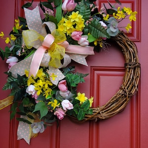 Couronne de vigne printanière ornée de tulipes, de jonquilles, de forsythia et d'une belle verdure qui ajoute de la texture.