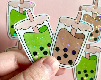 May include: Two holographic stickers of bubble tea with green and brown drinks. The stickers have a glittery finish and feature a straw and boba pearls.
