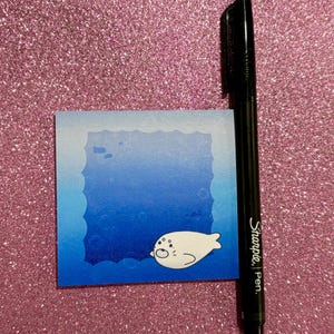 以下が含まれることがあります： 青い海の背景に、漫画のシールが泳いでいる、青と白の付箋。付箋はギザギザの縁取りがされている。