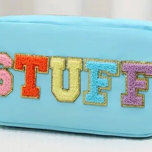 May include: A light blue zippered pouch with the word "STUFF" spelled out in colorful, fuzzy letters. The letters are outlined in gold.