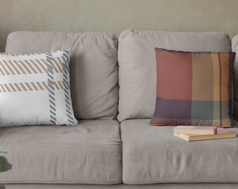 Könnte beinhalten: Zwei Kissen auf einem hellbraunen Sofa. Das Kissen links hat einen weißen Hintergrund mit braunem und grauem Karomuster. Das Kissen rechts hat ein rotes, braunes und graues Karomuster.